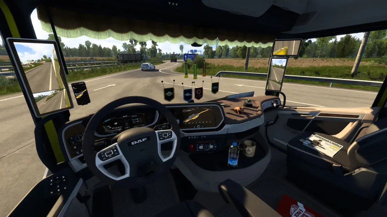 Wnętrze ciężarówki z widokiem na drogę. Na desce rozdzielczej widoczne są różne cabin accessories ets2, w tym nawigacja, telefon i ozdoby.