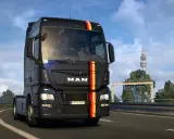 Ciemny MAN z niemieckimi barwami na masce jedzie autostradą. W tle wieża telewizyjna, typowa dla krajobrazu w grze german truck simulator.