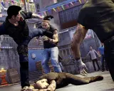 Akcja z gry Sleeping Dogs 2: uliczna bójka, jeden z bohaterów kopie przeciwnika, inni leżą na ziemi.