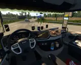 Wnętrze ciężarówki z widokiem na drogę. Na desce rozdzielczej widoczne są różne cabin accessories ets2, w tym nawigacja, telefon i ozdoby.