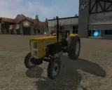Żółty Ursus C-360 FS17 na placu przed budynkami.