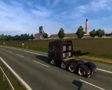 Ciemnobrązowa ciężarówka jedzie na wschód autostradą obok kopalni i pola.