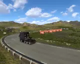 Ciężarówka jedzie krętą drogą w górach. W oddali widać małe czerwone domki i jezioro. To krajobraz z gry ETS2, prawdopodobnie z DLC.