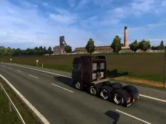 Ciemnobrązowa ciężarówka jedzie na wschód autostradą obok kopalni i pola.
