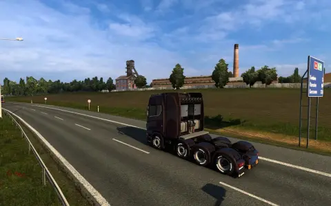 Ciemnobrązowa ciężarówka jedzie na wschód autostradą obok kopalni i pola.
