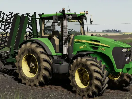 Zielony traktor John Deere 7730 z agregatem uprawowym, gotowy do pracy w polu w grze Ursus FS19.