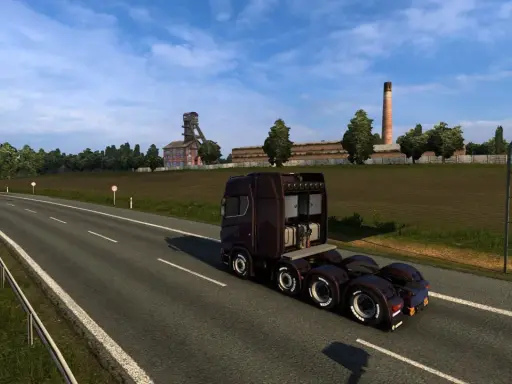 Ciemnobrązowa ciężarówka jedzie na wschód autostradą obok kopalni i pola.