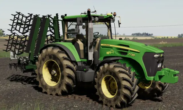 Zielony traktor John Deere 7730 z agregatem uprawowym, gotowy do pracy w polu w grze Ursus FS19.