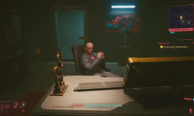 W cyberpunkowym domu lalek, Woodman siedzi w fotelu, groźnie patrząc. Na biurku leży klawiatura, a obok smoczy posąg.