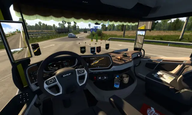 Wnętrze ciężarówki z widokiem na drogę. Na desce rozdzielczej widoczne są różne cabin accessories ets2, w tym nawigacja, telefon i ozdoby.