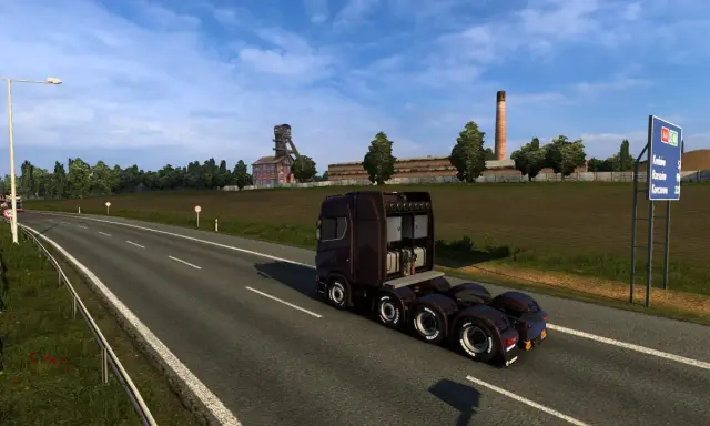 Ciemnobrązowa ciężarówka jedzie na wschód autostradą obok kopalni i pola.