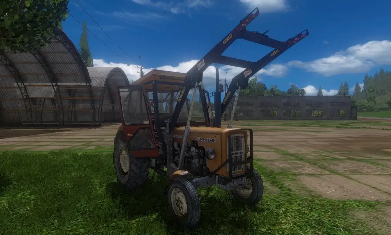 Ż&oacute;łty Ursus C360 FS17 z ładowaczem czołowym stoi na trawie przed hangarami.