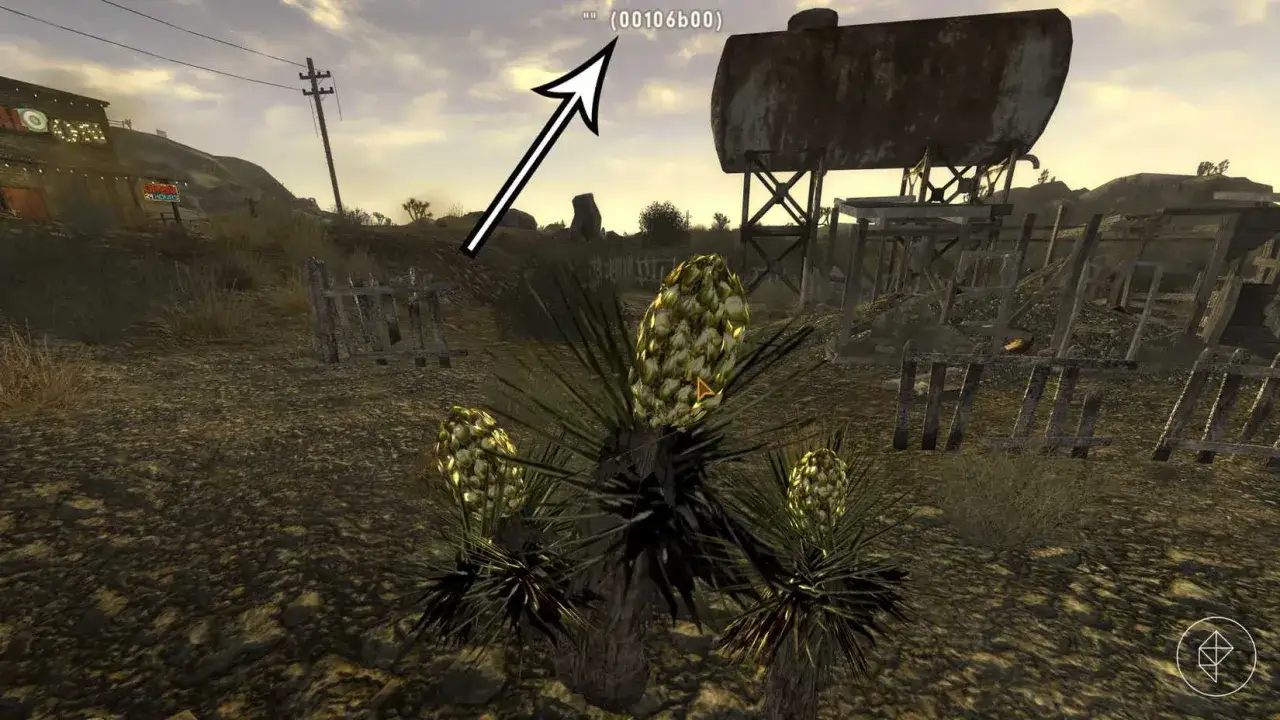Pustynia z roślinami i zniszczonymi budynkami. Strzałka wskazuje na ekran, gdzie widać kod (00106b00) z gry Fallout New Vegas kody.