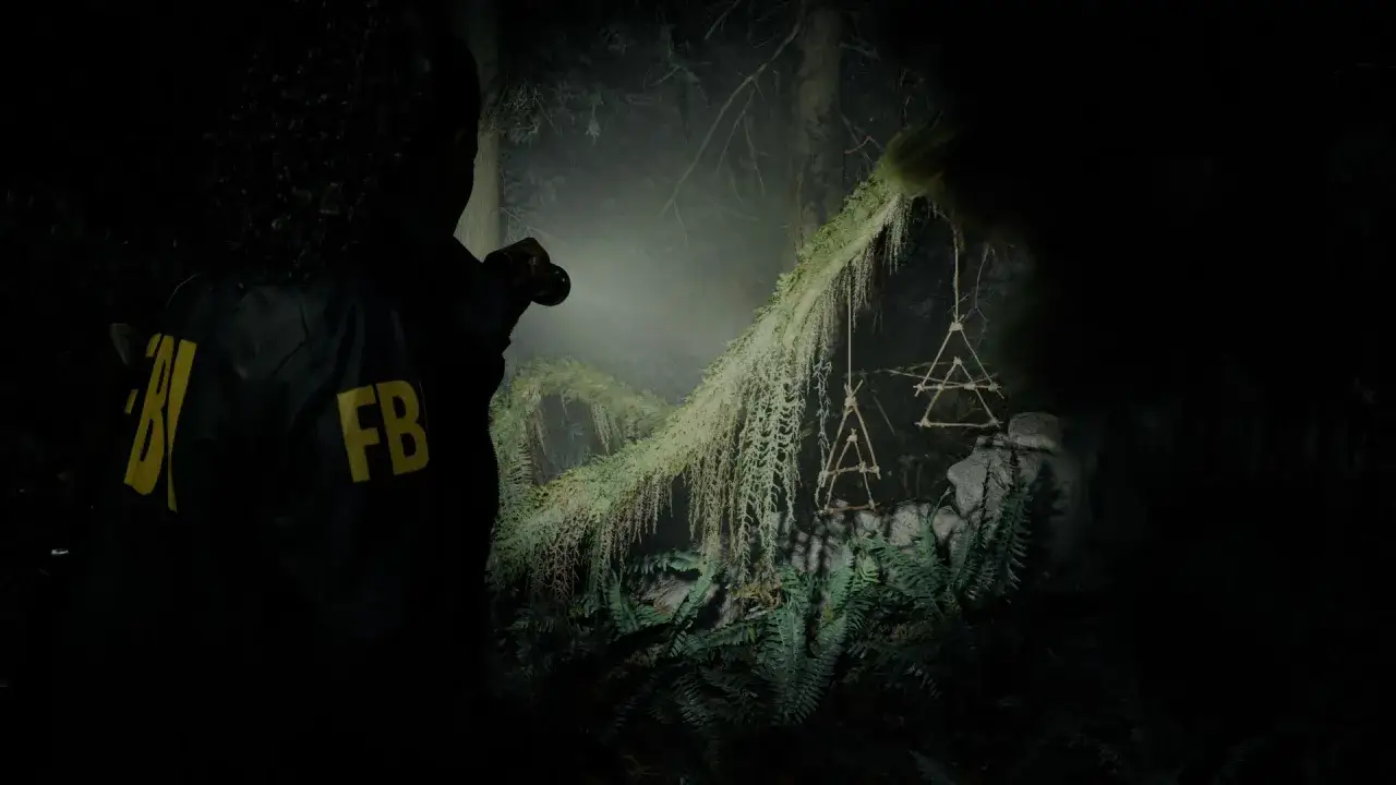 Agent FBI w mrocznym lesie, oświetlając latarką dziwne symbole. To kluczowy moment w alan wake 2 poradnik.