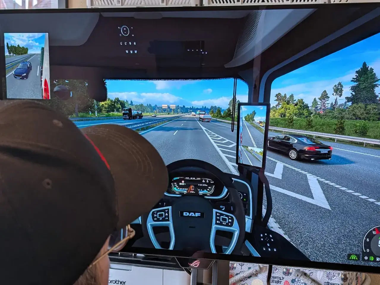 Gracz w czapce steruje ciężar&oacute;wką w grze ets2 scs. Widok z kabiny na autostradę, inne pojazdy i drzewa.
