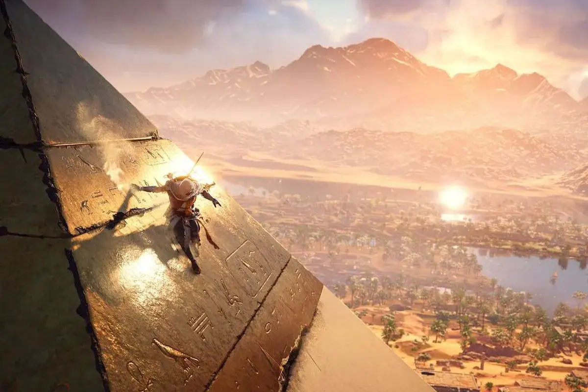 Bayek wspina się po piramidzie, szukając wskaz&oacute;wek w Assassin's Creed Origins poradnik. Słońce zachodzi nad pustynią.